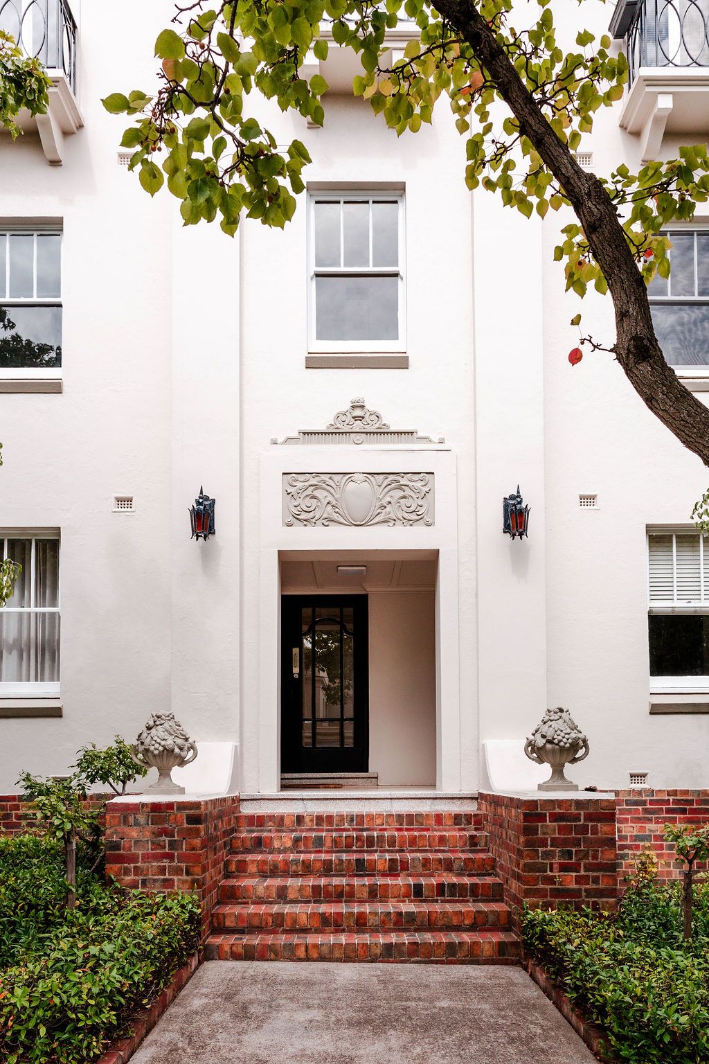 Entrance to the Toorak showroom, a portrait of a vibrant red brick stairway leading to an antique white building, adorned by greenery
